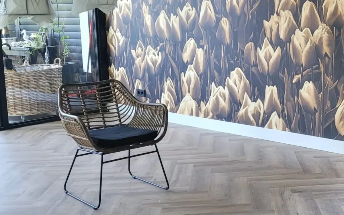Lichte visgraatvloer met witte plinten, tulpenbehang en een rotan fauteuil